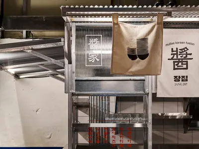 極簡餐廳室內，設有金屬餐檯、木製長椅及韓文招牌。