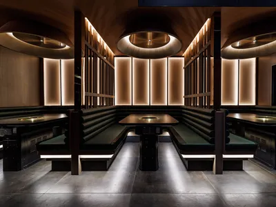 Modern restaurant booths with black leather seating, illuminated by warm, recessed lighting, and designed with sleek wood fur