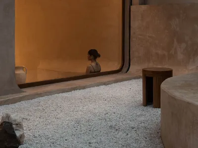 A modern restaurant exterior with a minimalist design, featuring a concrete exterior and a large glass window.