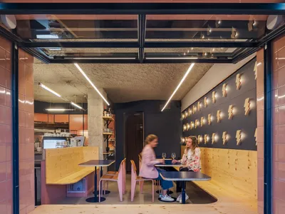 People sitting at a cafe with wooden tables, concrete columns, and terrazzo flooring.