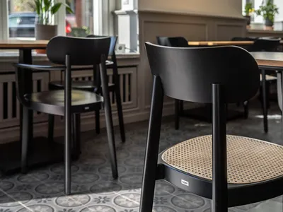 A cafe interior with wooden furniture, including black chairs with woven seats and wooden tables.