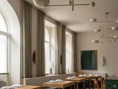 A modern restaurant interior featuring concrete tables and archways with large windows.