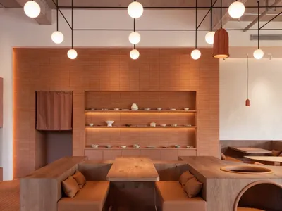 A modern restaurant interior with terracotta walls and wooden seating and fixtures.