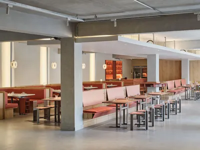 A well-designed modern restaurant with exposed concrete ceiling, red seats, and metallic tables.