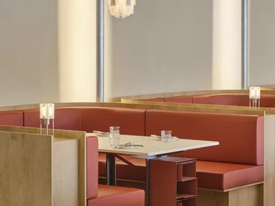 Modern industrial-style restaurant interior with red leather booths, white table, and geometric lighting fixture.