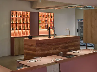 A modern bar with a marble counter featuring illuminated shelves filled with various bottles.
