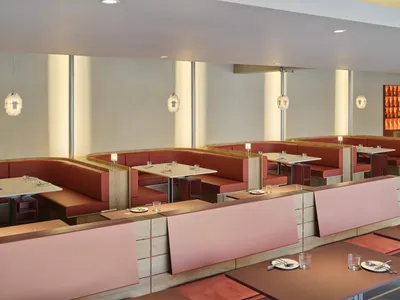 A modern restaurant interior featuring red booth seating with wooden accents and glass pendant lights.
