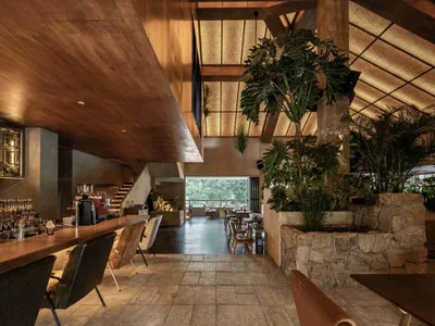 A modern restaurant with a wooden ceiling, stone bar, and concrete flooring, featuring a concrete bar counter and stone walls