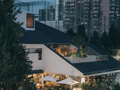 A modern restaurant exterior with concrete walls and a roof garden, surrounded by tall buildings and trees.