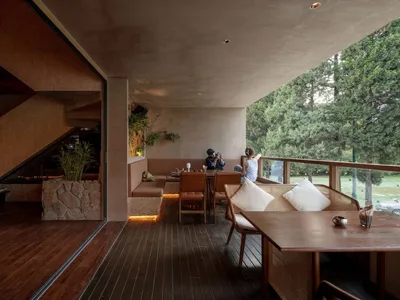 Modern restaurant interior with wooden tables, stone accents, and concrete seating