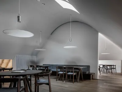 A minimalist restaurant interior with gray walls, wooden tables, and pendant lights.
