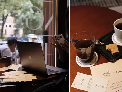 A coffee shop scene featuring a wooden table with a cup of coffee and a slice of cake, next to a laptop and a smartphone.