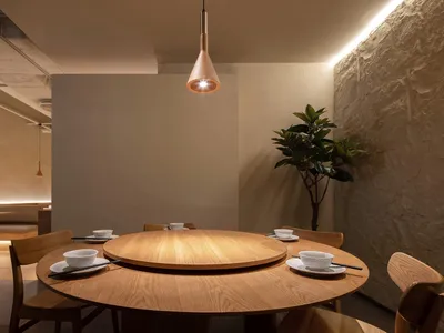 A round dining table in a modern restaurant interior, surrounded by wooden chairs and featuring a central lazy susan.