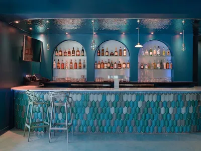 A modern bar with blue ceramic tile walls, a curved countertop, and various bottles of alcohol on shelves.