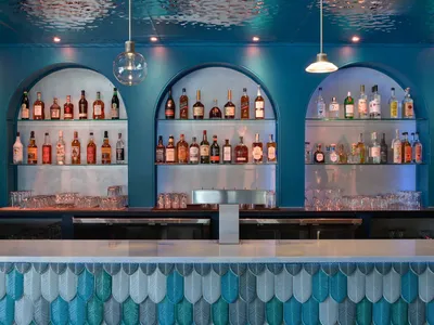 A photograph of a modern bar counter featuring glass shelves with various bottles of liquor.