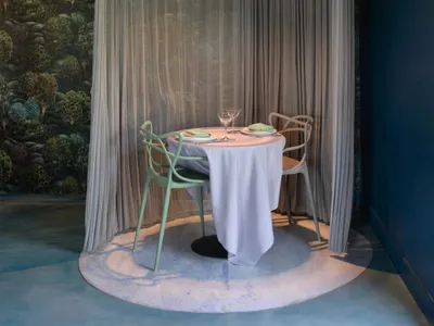 A modern restaurant booth with a white tablecloth, green chairs, and a fabric curtain.