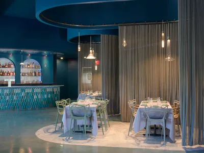 A modern, industrial interior design of a restaurant featuring metallic finishes, glass elements, and translucent curtains.