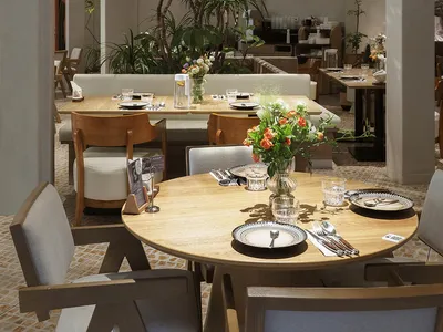 Modern restaurant interior with wooden tables, glass vases, and plush fabric chairs.