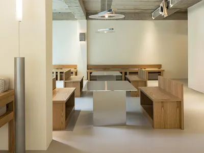 Modern minimalist restaurant interior featuring wooden benches and tables.