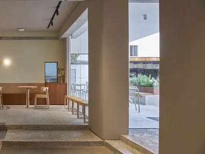 A modern restaurant interior featuring wooden tables, glass partitions, and a concrete floor