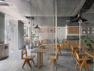 Modern restaurant interior featuring wooden tables and chairs, concrete floors, and industrial lighting.