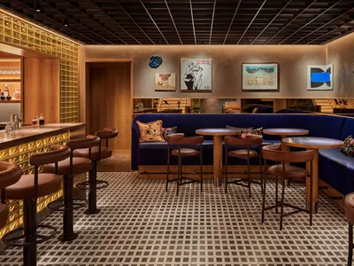 A contemporary restaurant bar featuring wooden furniture, glass walls, and upholstered seating.