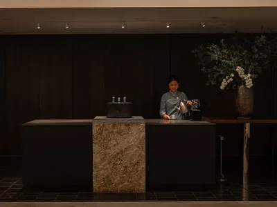 A hotel reception desk featuring granite and marble materials with wooden accents and a person working on it.