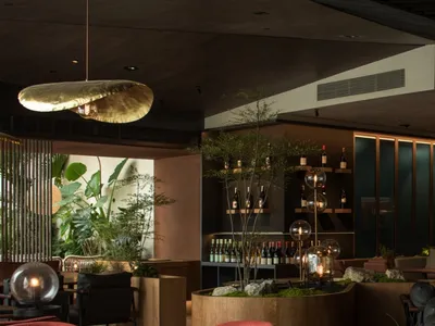 Modern restaurant bar with wood and concrete finishes, featuring elegant seating and a well-stocked bar.