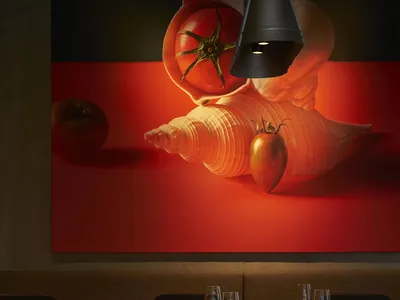 Modern restaurant interior with wooden tables, red lighting, and large tomato mural