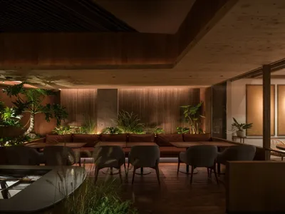A modern restaurant interior with wooden seating, concrete accents, and lush green plants.
