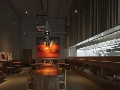 Modern restaurant interior with long wooden tables and metallic elements, featuring a minimalist design with large artwork on