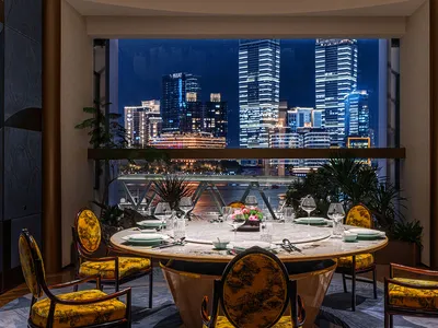 A luxurious dining room featuring marble, glass, and yellow elements with a stunning city view at dusk.