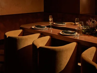 A modern restaurant dining room with wood furniture and a long table set for four.