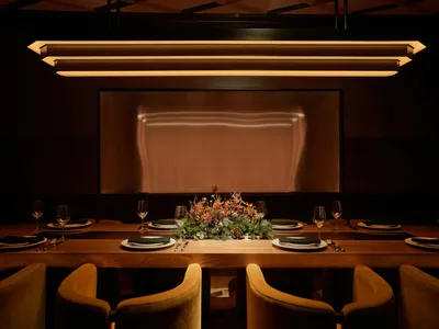 A modern restaurant dining room featuring a long wooden table, each place setting includes a glass of wine, plates, forks and