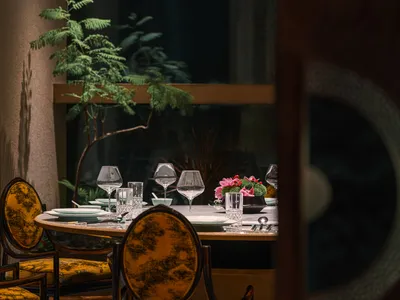 A modern restaurant dining table set with glassware, porcelain plates, and cutlery, surrounded by yellow upholstered chairs a