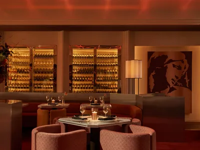 A warmly lit restaurant interior with a wine bar featuring modern furniture and a variety of bottles on display.