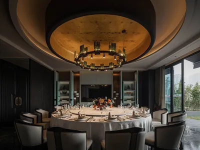 Luxurious dining room with glass paneling, round table, black and white chairs, and hanging chandelier.