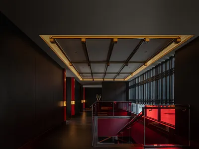 Modern hotel lobby featuring black walls, wooden beams, metal roofing, and red lighting.