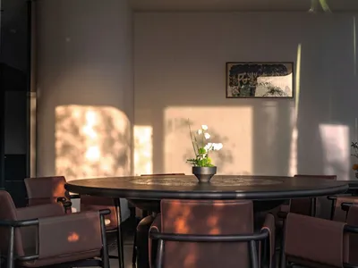 A well-lit, modern restaurant interior with a round dining table, brown leather chairs, and a potted plant.