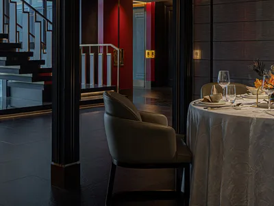 Modern restaurant interior with red walls and marble flooring featuring a dining table set for two.