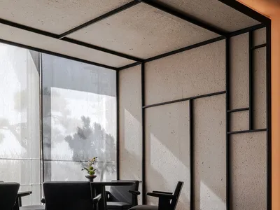 A minimalist hotel lobby interior featuring concrete walls and floor, black furniture, and a large window.