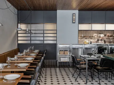 Industrial restaurant dining area with wooden furniture, metal counter, and black and white floor pattern