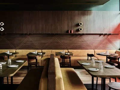 A modern restaurant interior with wooden tables, leather benches, and contemporary lighting fixtures.