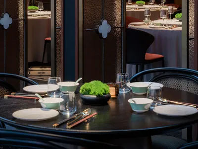 A modern restaurant interior with black and white tables, wooden accents, and greenery.