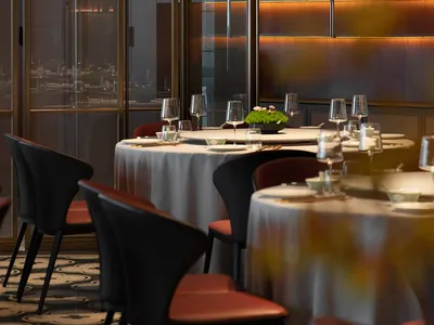 A modern restaurant interior featuring dark wood, glass, and marble materials, with tables set for dining.