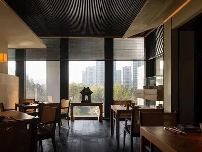 Modern restaurant dining area with concrete walls, wooden tables, and black wooden blinds.