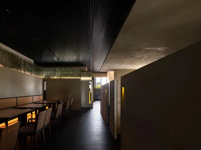 Modern restaurant interior with wooden tables, concrete walls, and warm lighting.