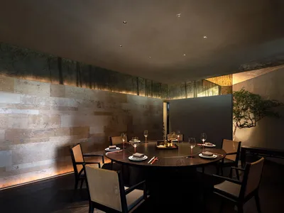 Modern restaurant interior with wood and marble materials, featuring a round dining table with place settings and wine glasse