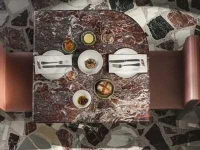 A restaurant table with a marble tabletop, set with plates, cutlery, and bread.