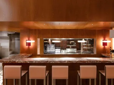 A modern minimalist restaurant bar with a marble countertop and stools.